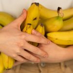 Crop unrecognizable person with bundles of tasty ripe bananas with pleasant aroma and spots on peel